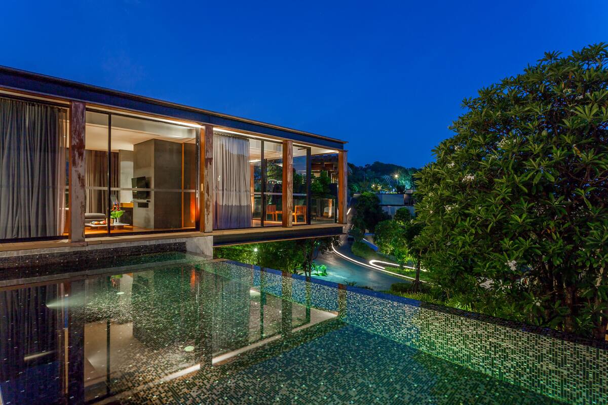 A modern house with a glass facade, a swimming pool with mosaic tiles, and lush greenery.