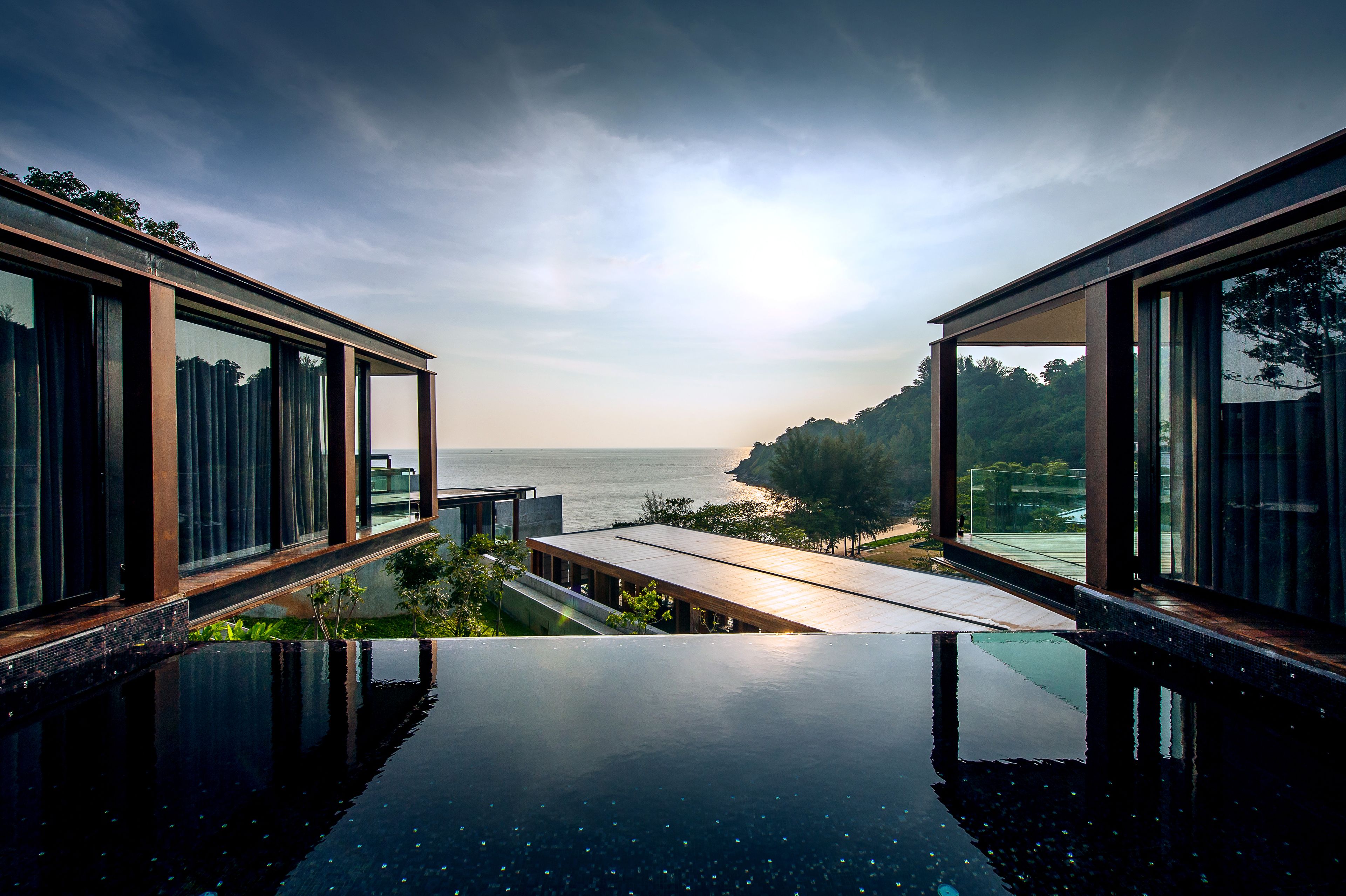 A modern infinity pool with a view of the sea and a wooden deck.