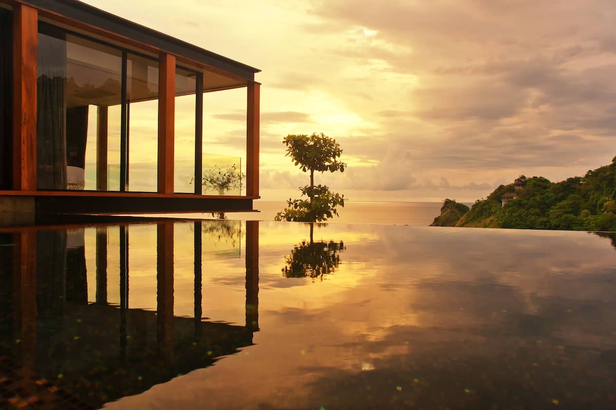 A modern building with large glass windows reflecting a sunset over a calm body of water.