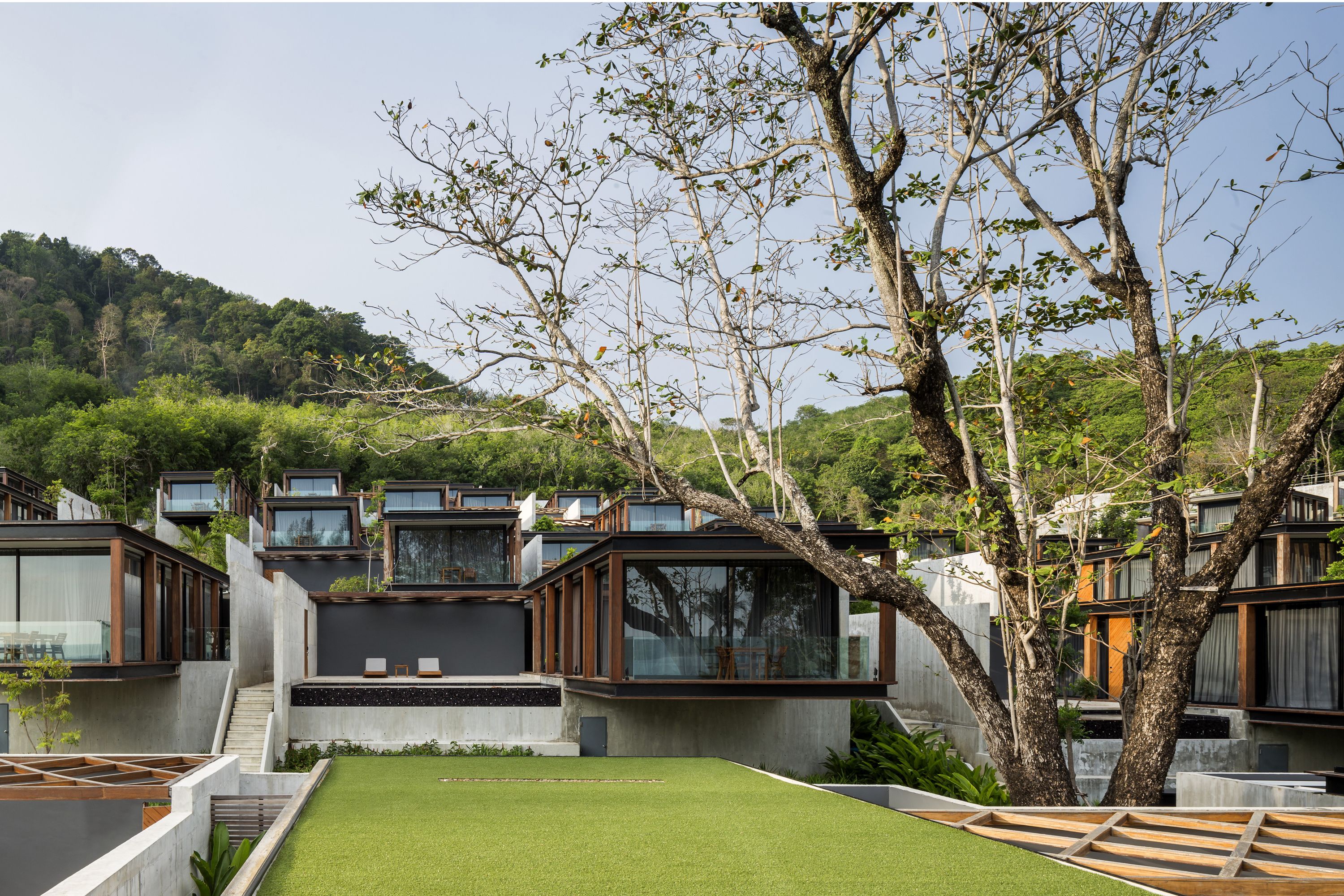 A modern residential complex with multiple houses featuring large windows, concrete structures, and a well-maintained lawn.
