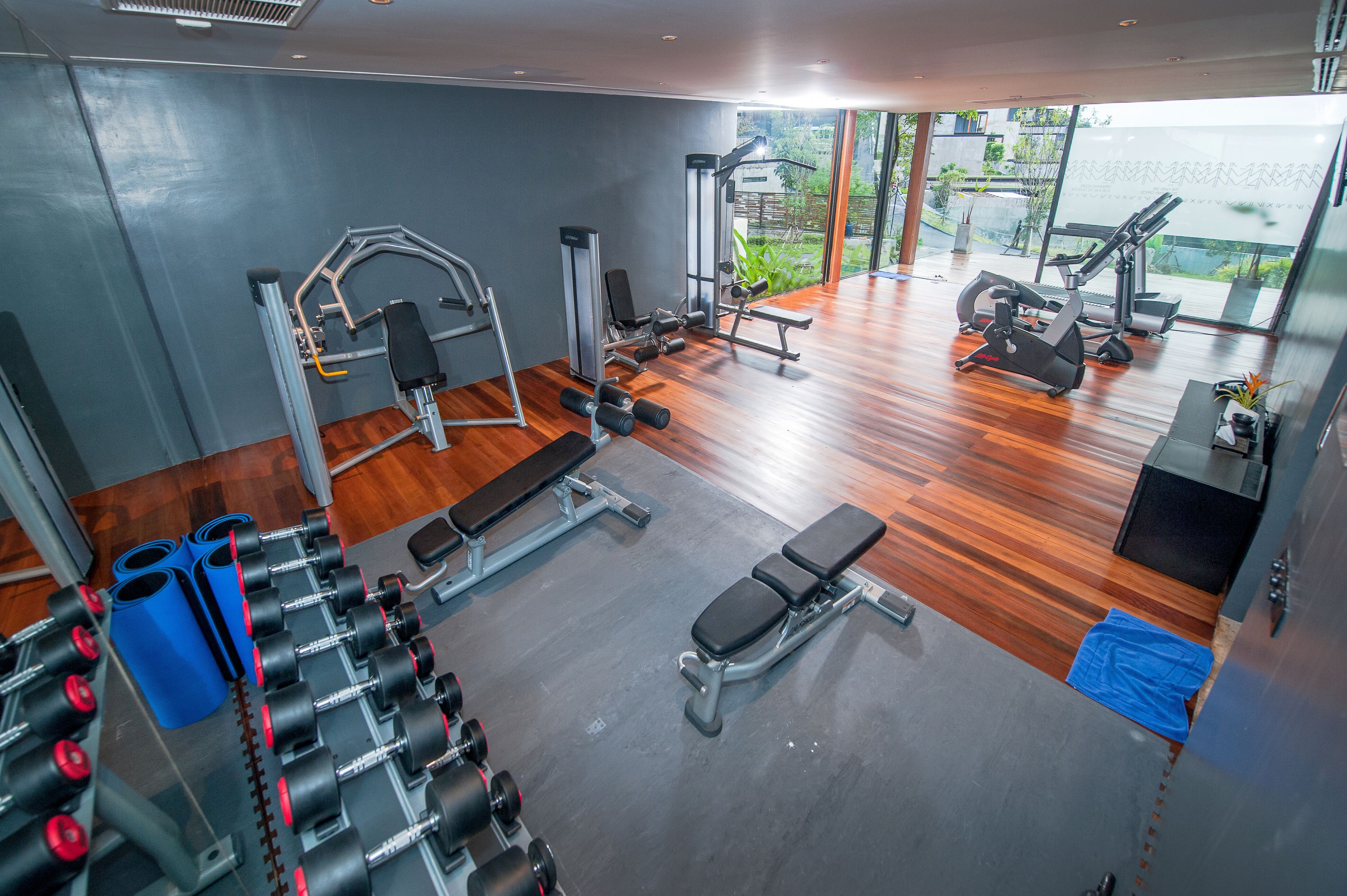 Un gimnasio con diferentes máquinas de ejercicio, una banca y vistas a zonas verdes.