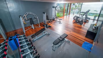 Un gimnasio con diferentes máquinas de ejercicio, una banca y vistas a zonas verdes.