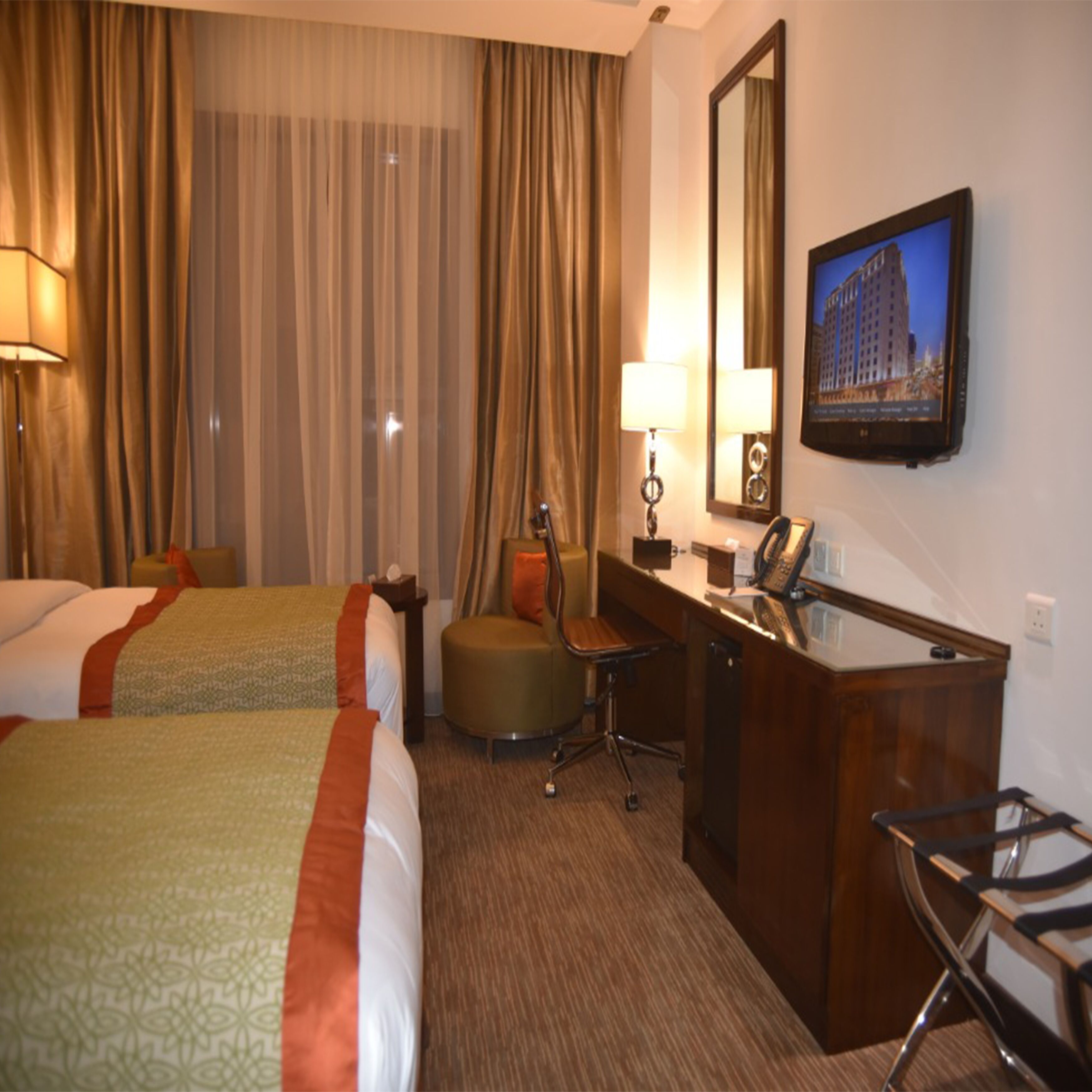 A hotel room with two beds, a desk with a telephone, a chair, a lamp, and a television on the wall.