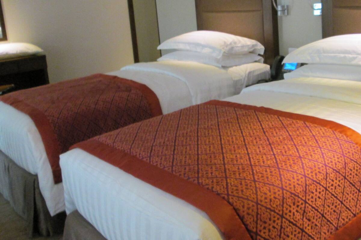 Ein Hotelzimmer mit zwei Betten, jeweils mit weißen Laken und orangefarbenen Decken. Ein hölzernes Kopfteil beherbergt ein Telefon und eine Lampe.