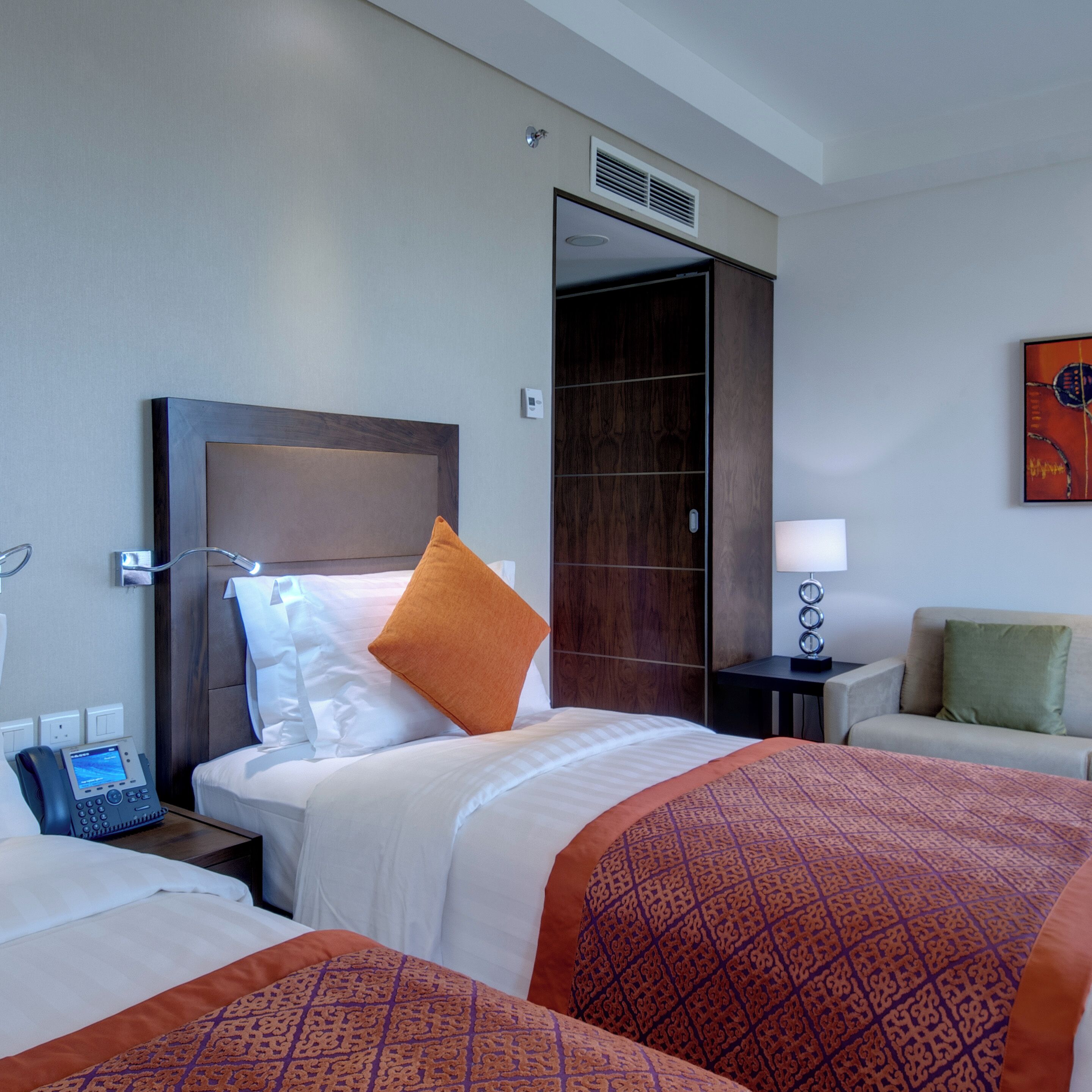 A hotel room with two beds, a bedside table with a phone, a lamp, and a painting on the wall.