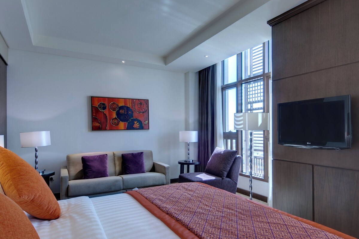 A hotel room with a large bed, two armchairs, a sofa, a flat-screen TV, and a painting on the wall.