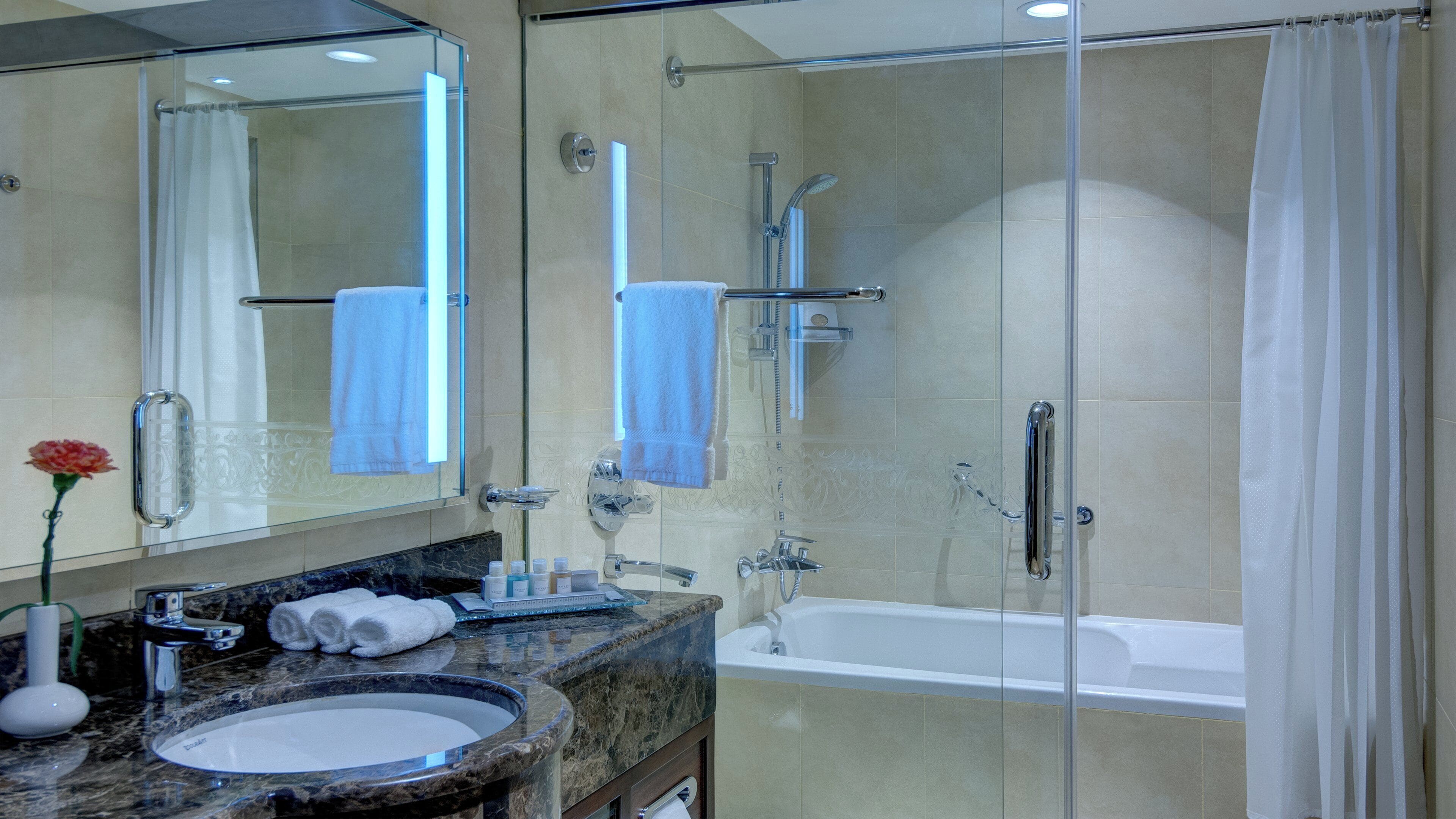 A bathroom with a glass-enclosed shower, a bathtub, a sink with a marble countertop, and a mirror.