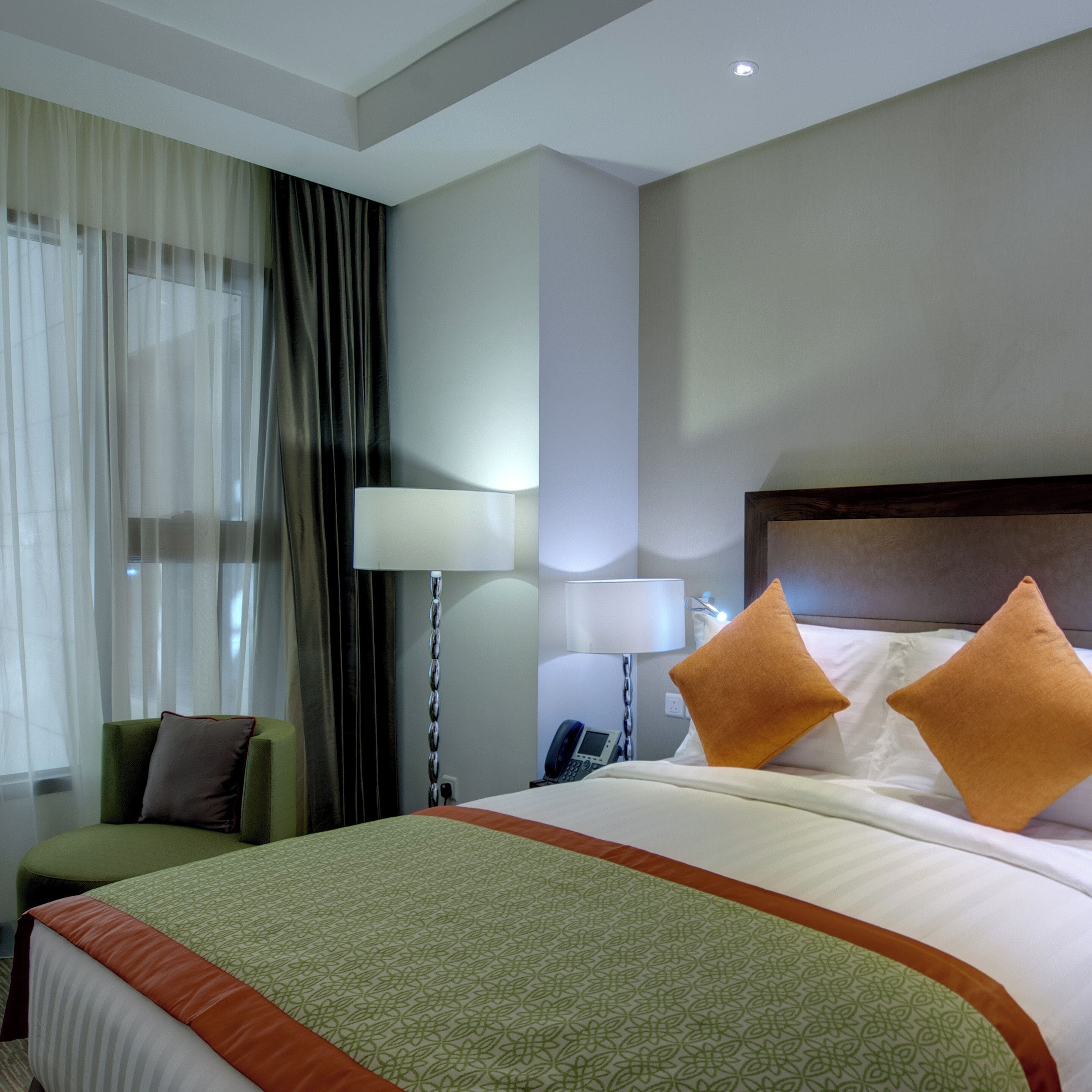 A hotel room with a bed, a chair, a lamp, and a nightstand.