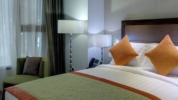 A hotel room with a bed, a chair, a lamp, and a nightstand.