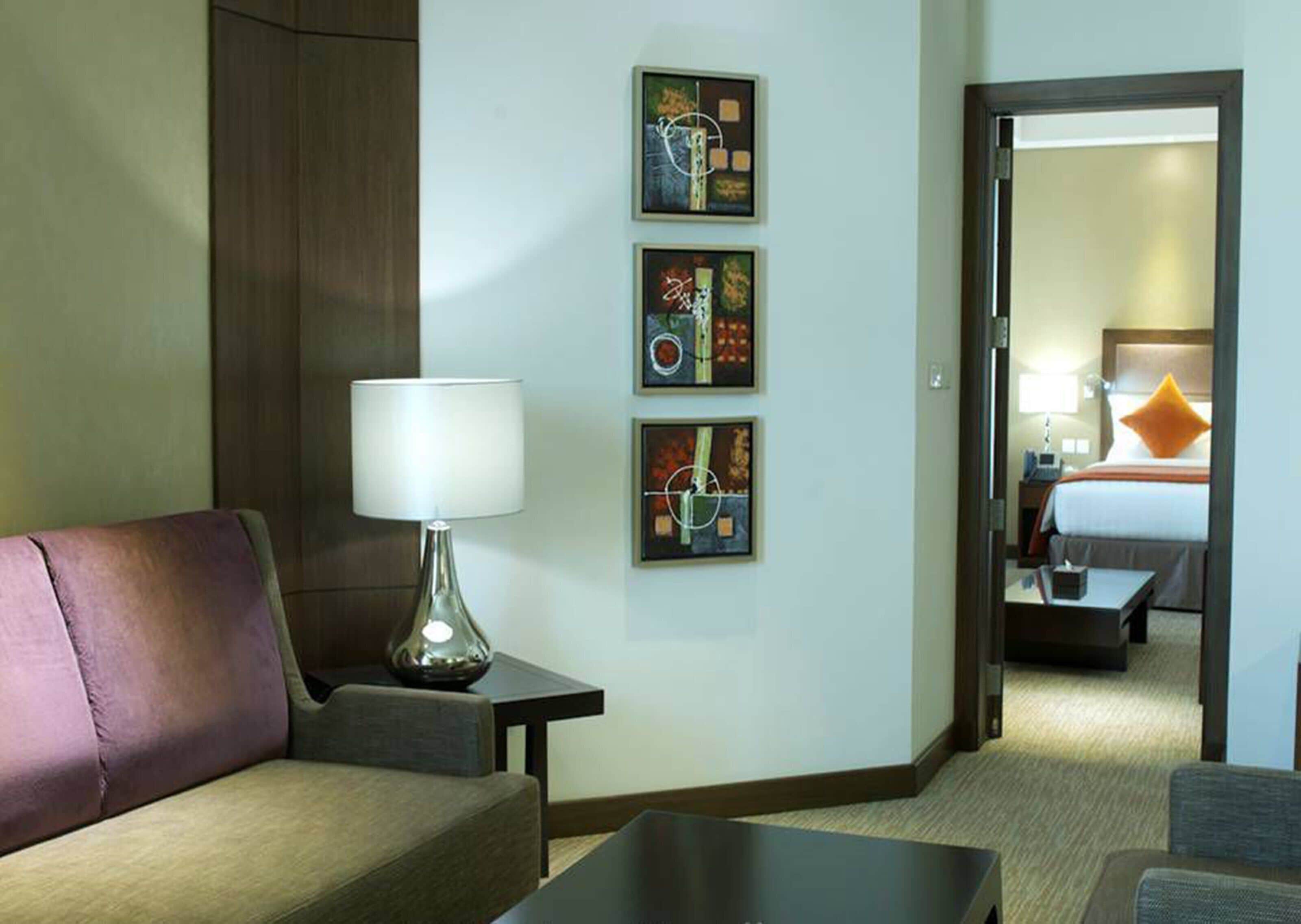 Een hotelkamer met een bank, een lamp en drie ingelijste kunstwerken aan de muur.