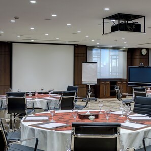 A conference room with round tables, chairs, a projector, and a screen. - Crowne Plaza Madinah by IHG (Madinah)