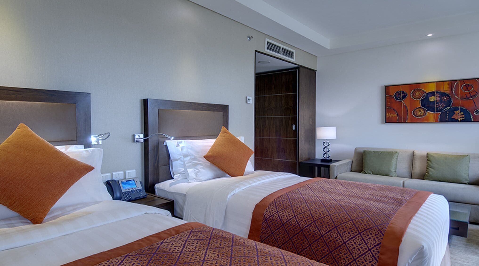 Une chambre d’hôtel avec deux lits, une table de chevet avec un téléphone, une lampe et un canapé.