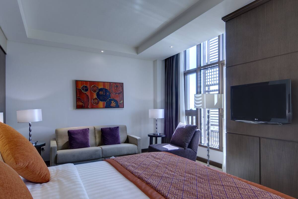 Ein Hotelzimmer mit einem großen Bett, zwei Sesseln, einem Sofa, einem Flachbildfernseher und einem Bild an der Wand.