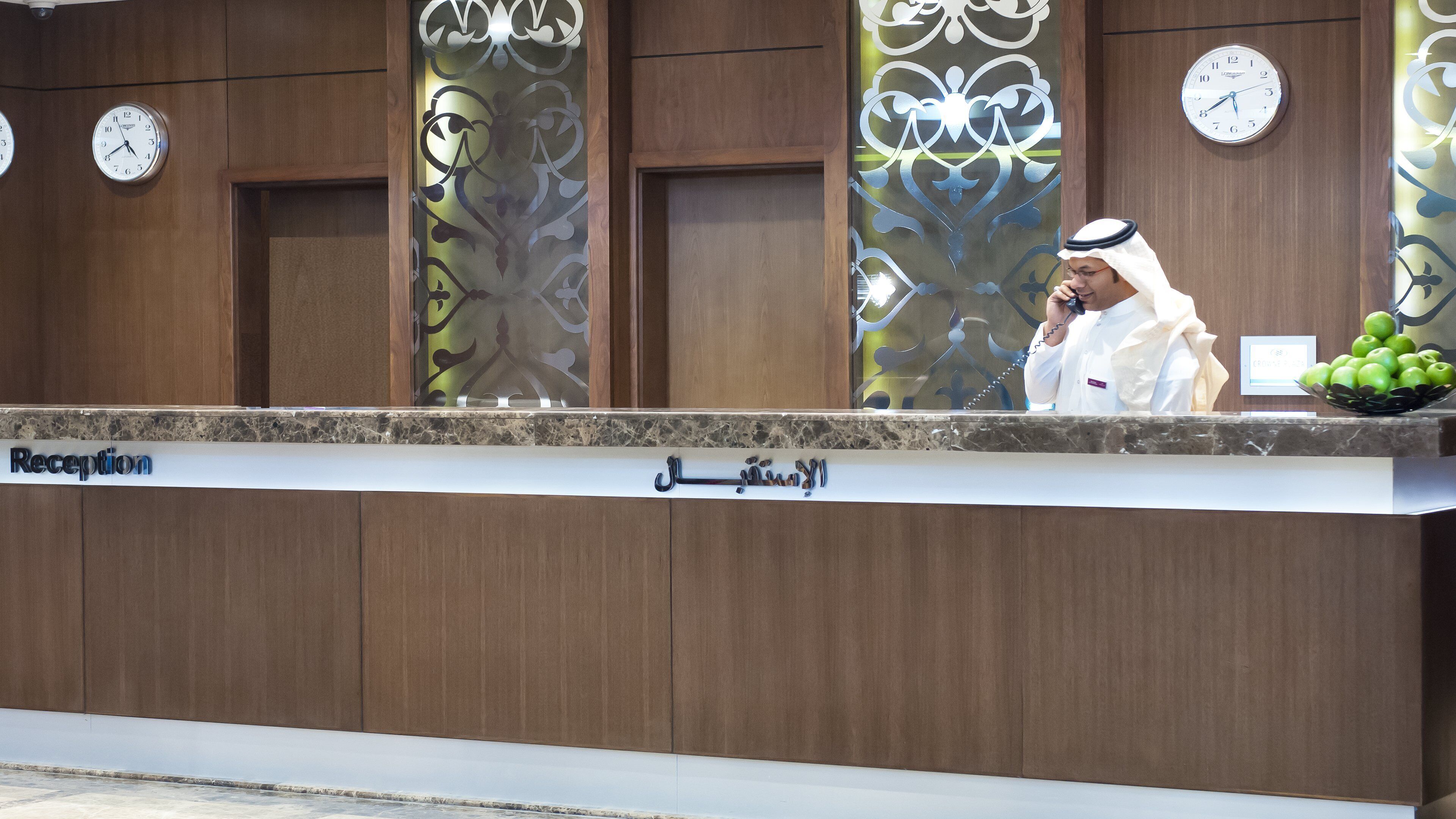 A reception desk with a marble top, wooden paneling, and clocks on the wall.