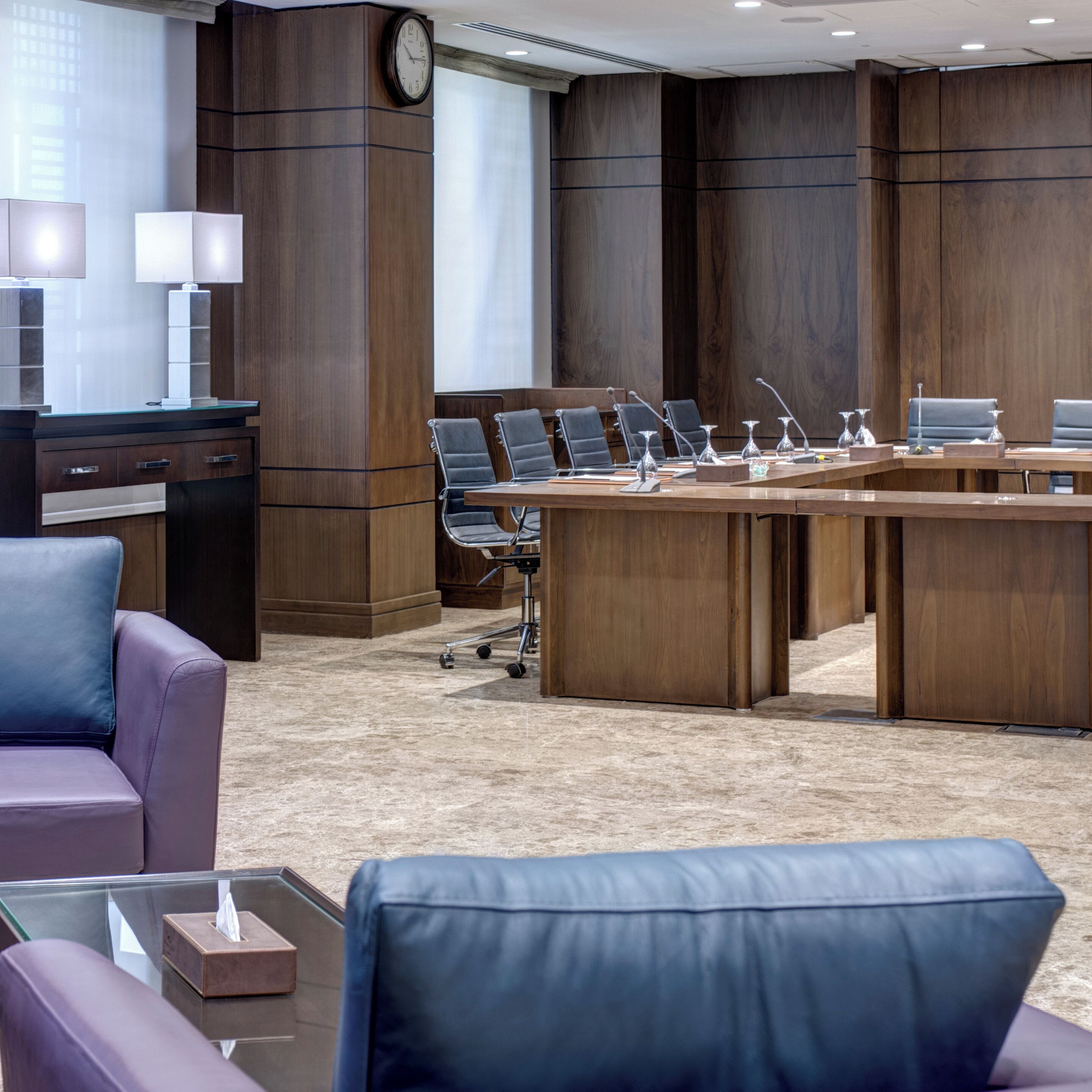 Une salle de conférence avec une grande table en bois, plusieurs chaises, une horloge et un bureau avec une lampe.