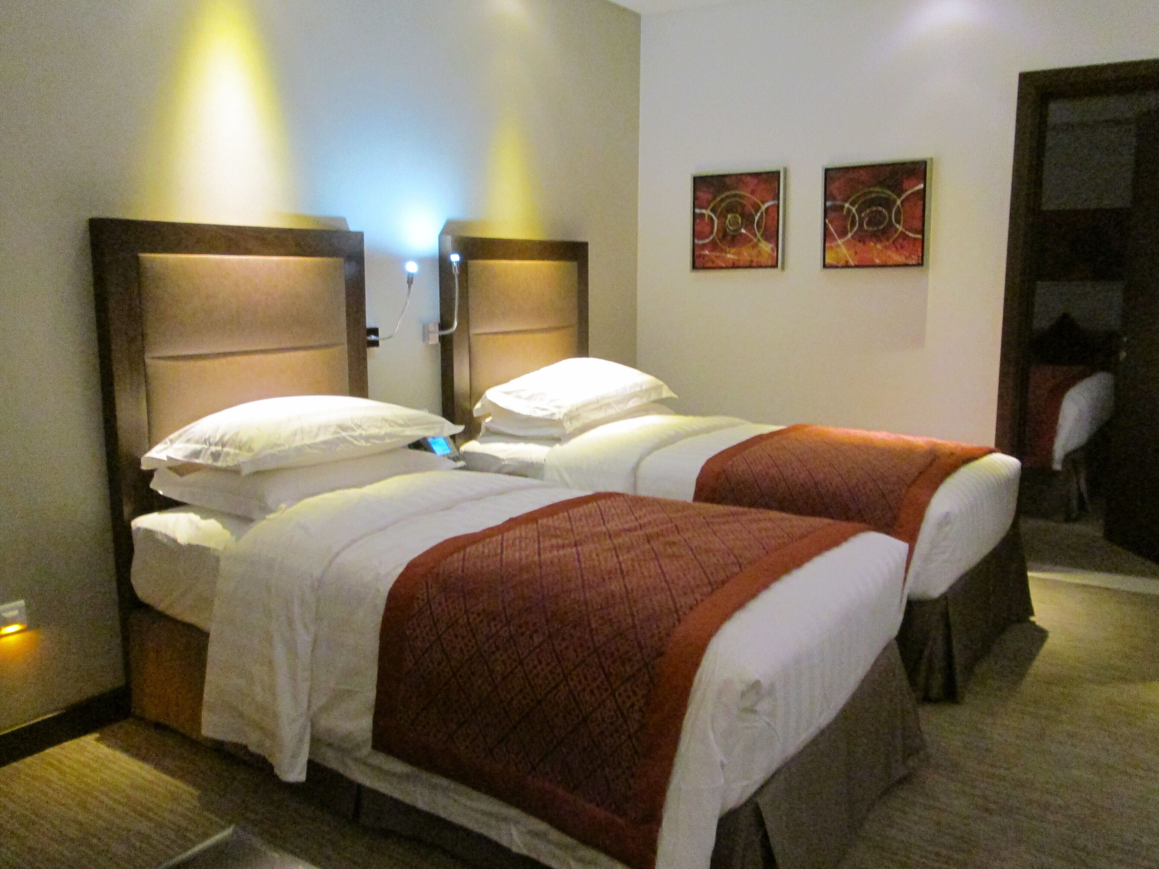 A hotel room with two single beds, a nightstand, and a wall-mounted lamp.