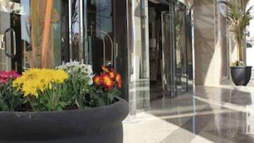 A modern building entrance with glass doors and a large planter with flowers.
