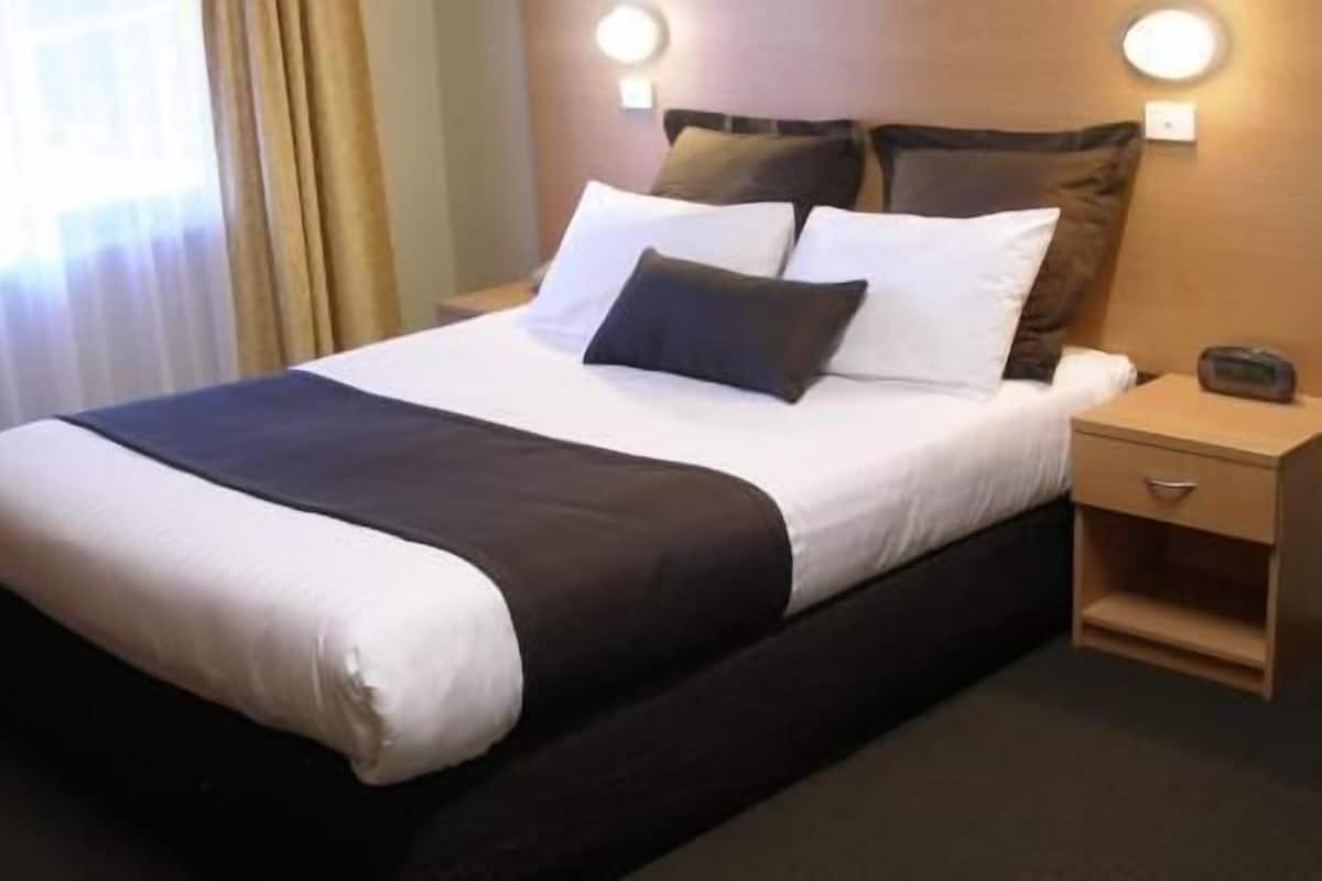 Una habitación de hotel con una cama, una mesita de noche y otra mesita auxiliar.