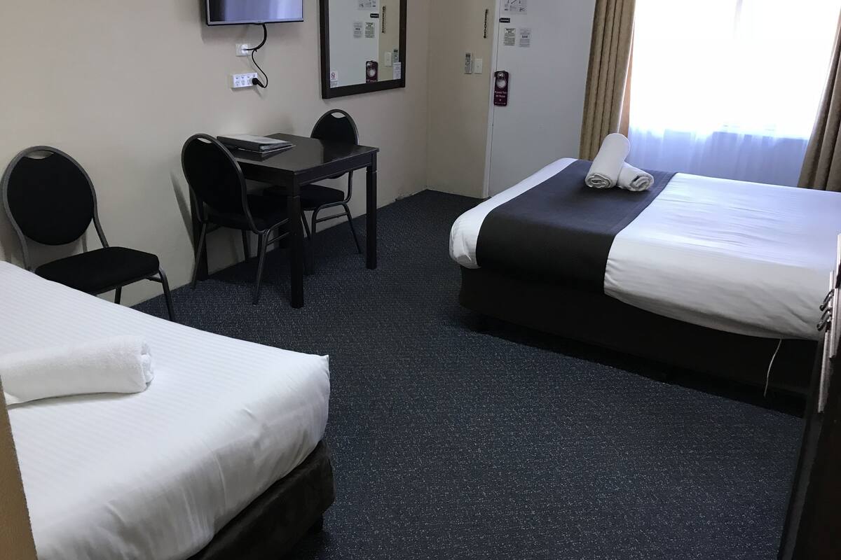 A hotel room with two beds, a desk, a chair, a TV, and a window with curtains.