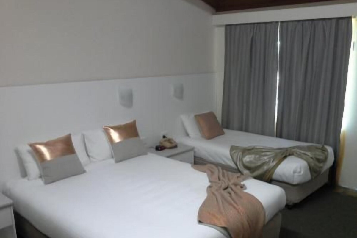 A hotel room with two beds, a nightstand, and a window with curtains.