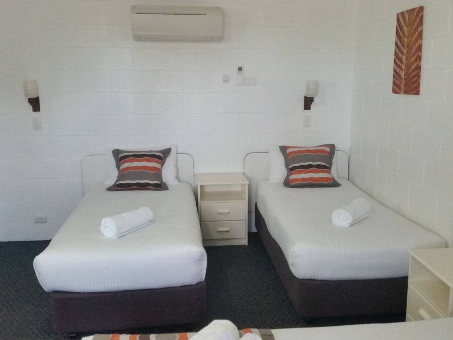 A twin room with two beds, each with a pillow and a rolled towel. There is a small bedside table and a wall-mounted air conditioner.