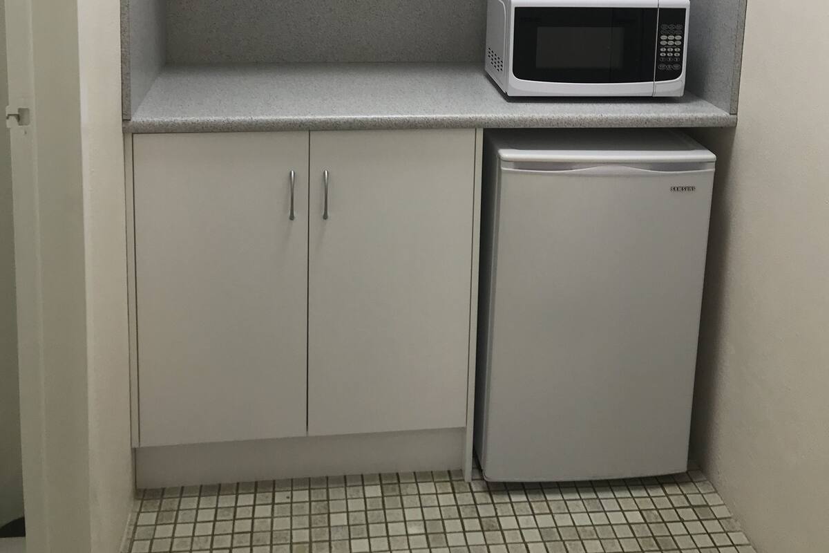 A compact kitchenette with white cabinets, a microwave, and a small refrigerator.