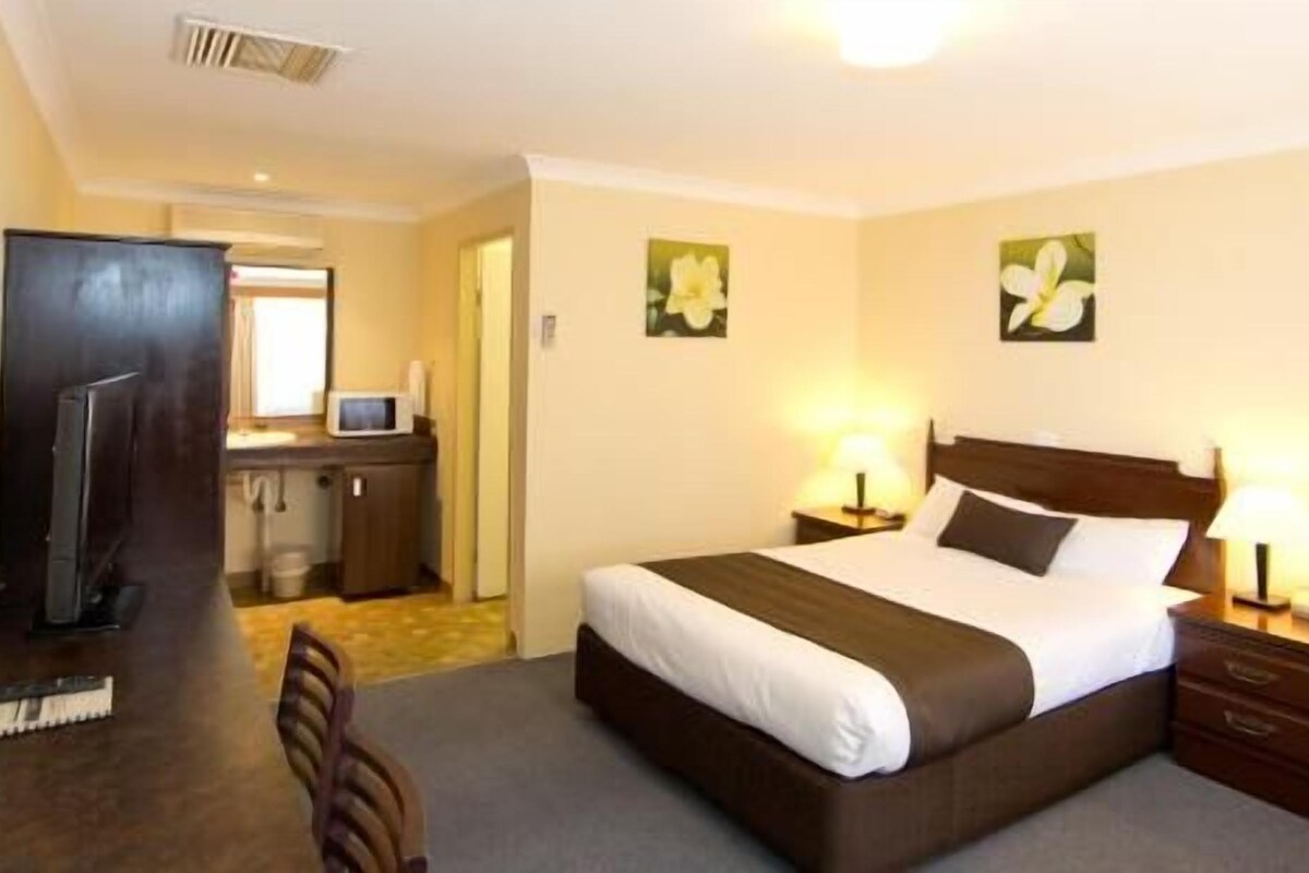 A hotel room with a bed, bedside tables, a desk with a microwave, and a TV.