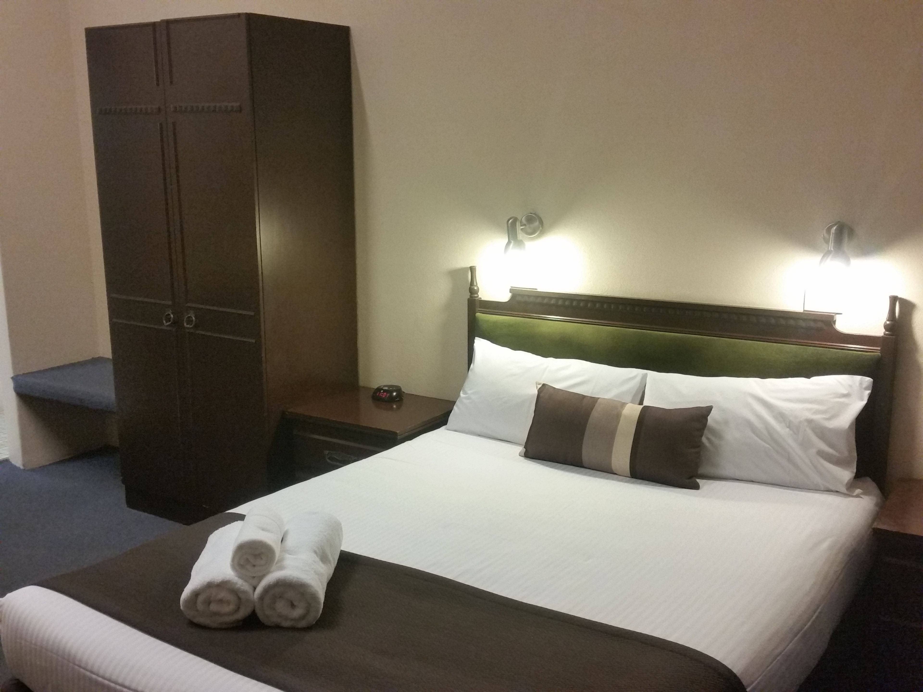 A hotel room with a bed, a wardrobe, and a nightstand.