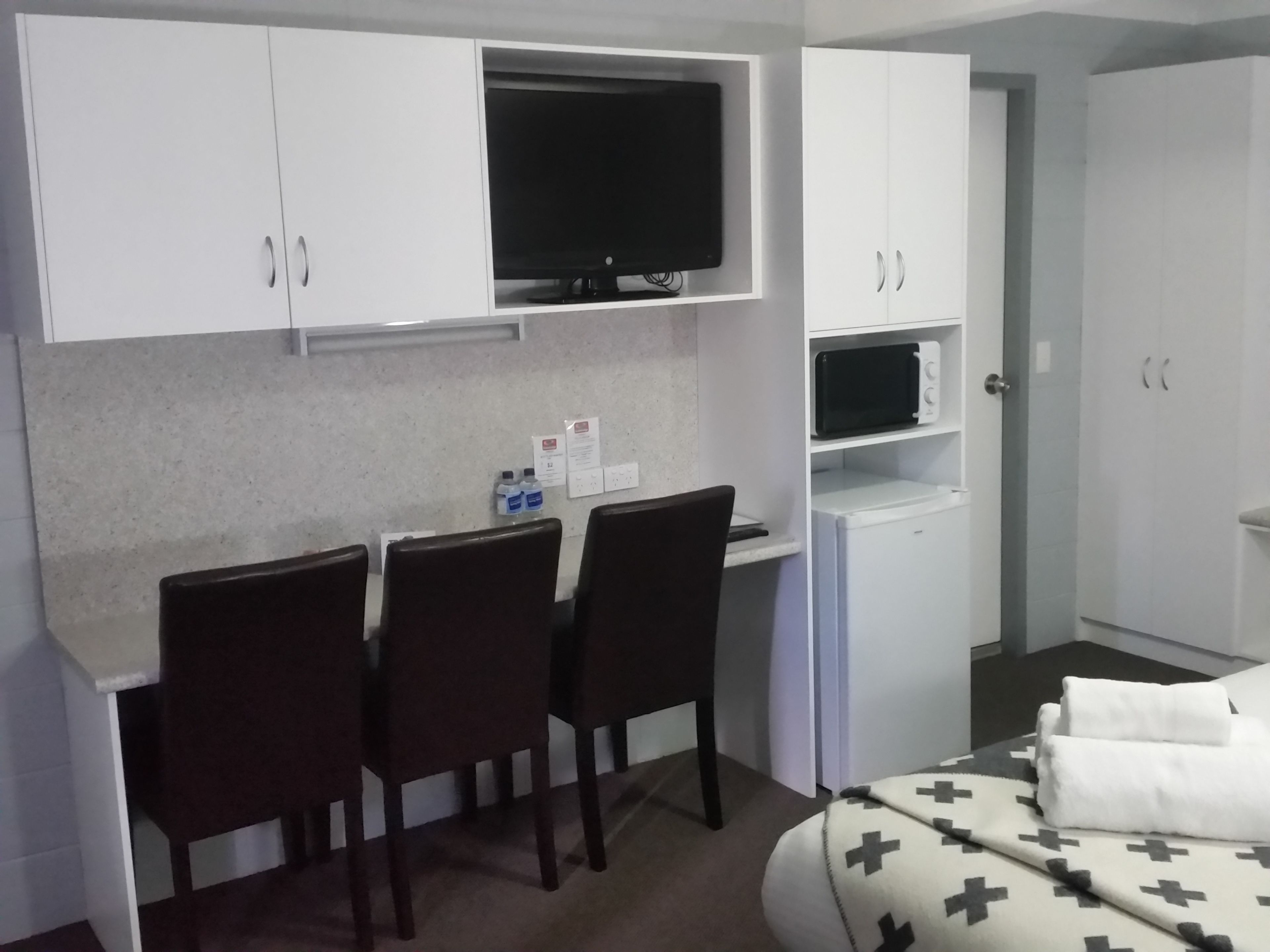 A bedroom with a bed, a desk with a chair, a TV, a microwave, and a small refrigerator.