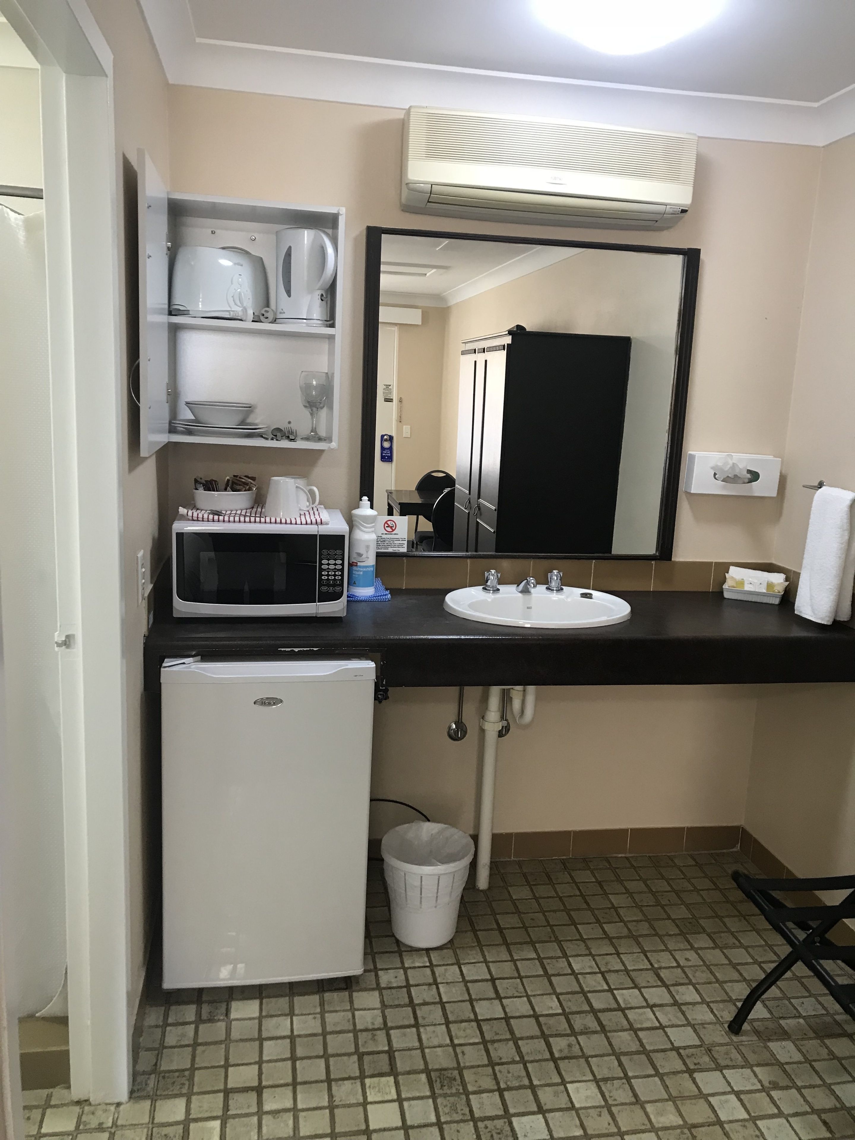 A compact bathroom with a sink, mirror, microwave, and a small refrigerator.