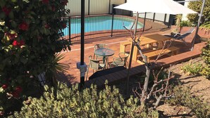 A backyard with a swimming pool, patio furniture, and a wooden deck.