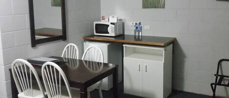 A small kitchenette with a microwave, a sink, and a cabinet. There are two white chairs and a table.