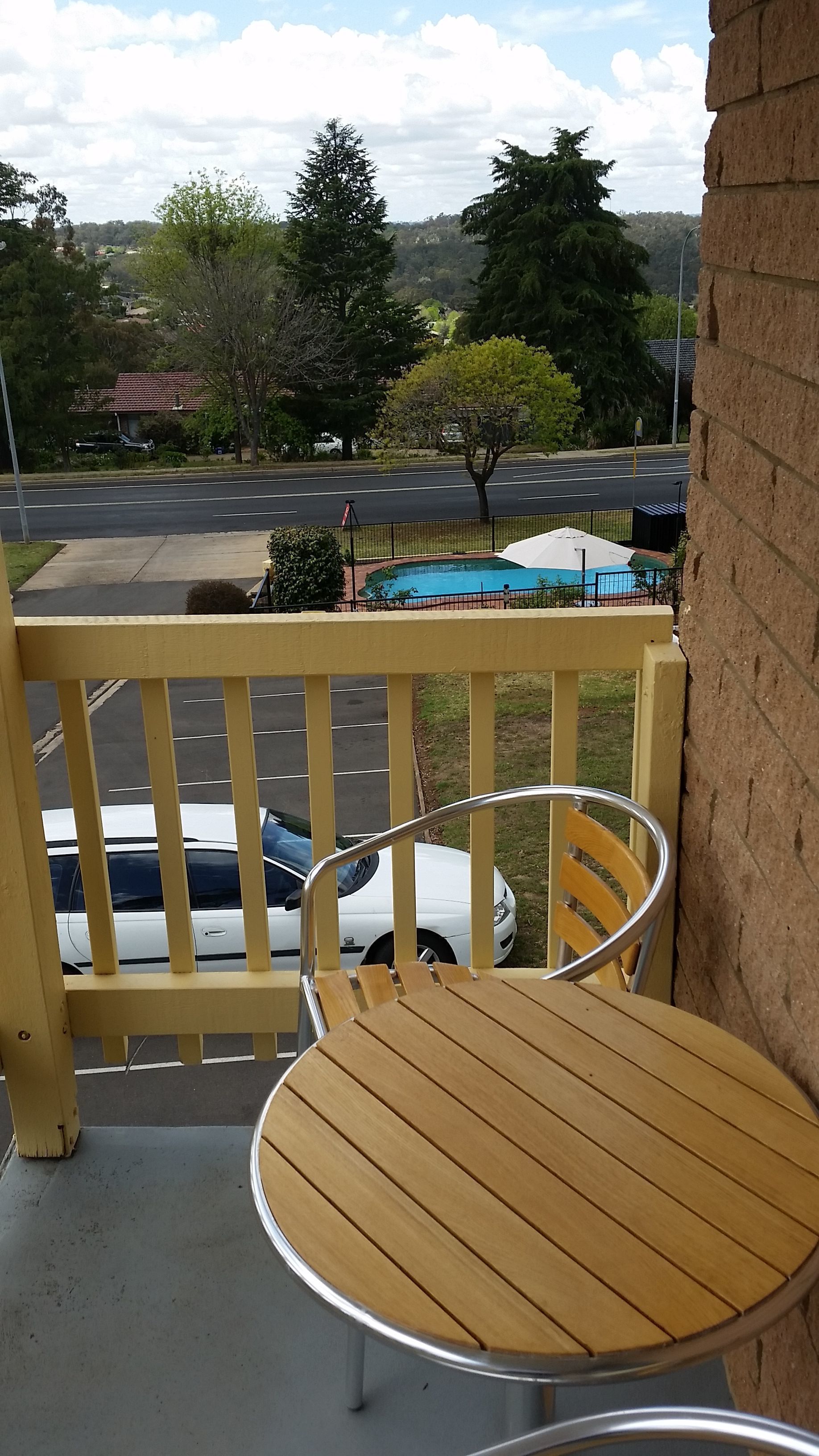 Une chaise et une table en bois sur un balcon, avec vue sur une route et des arbres.