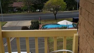 A wooden chair and table on a balcony with a view of a road and trees.