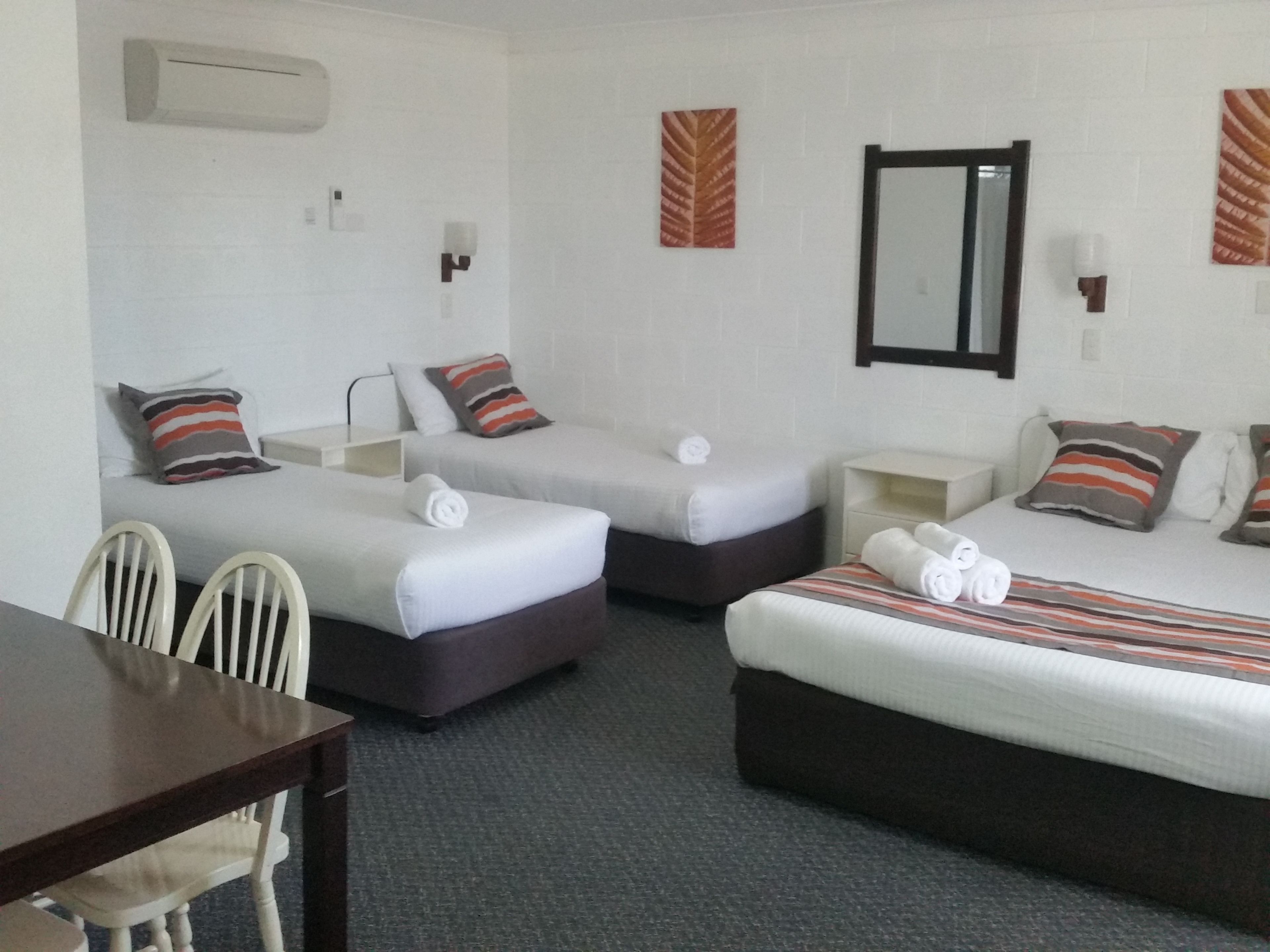 A hotel room with two single beds, a double bed, a desk, and a chair.