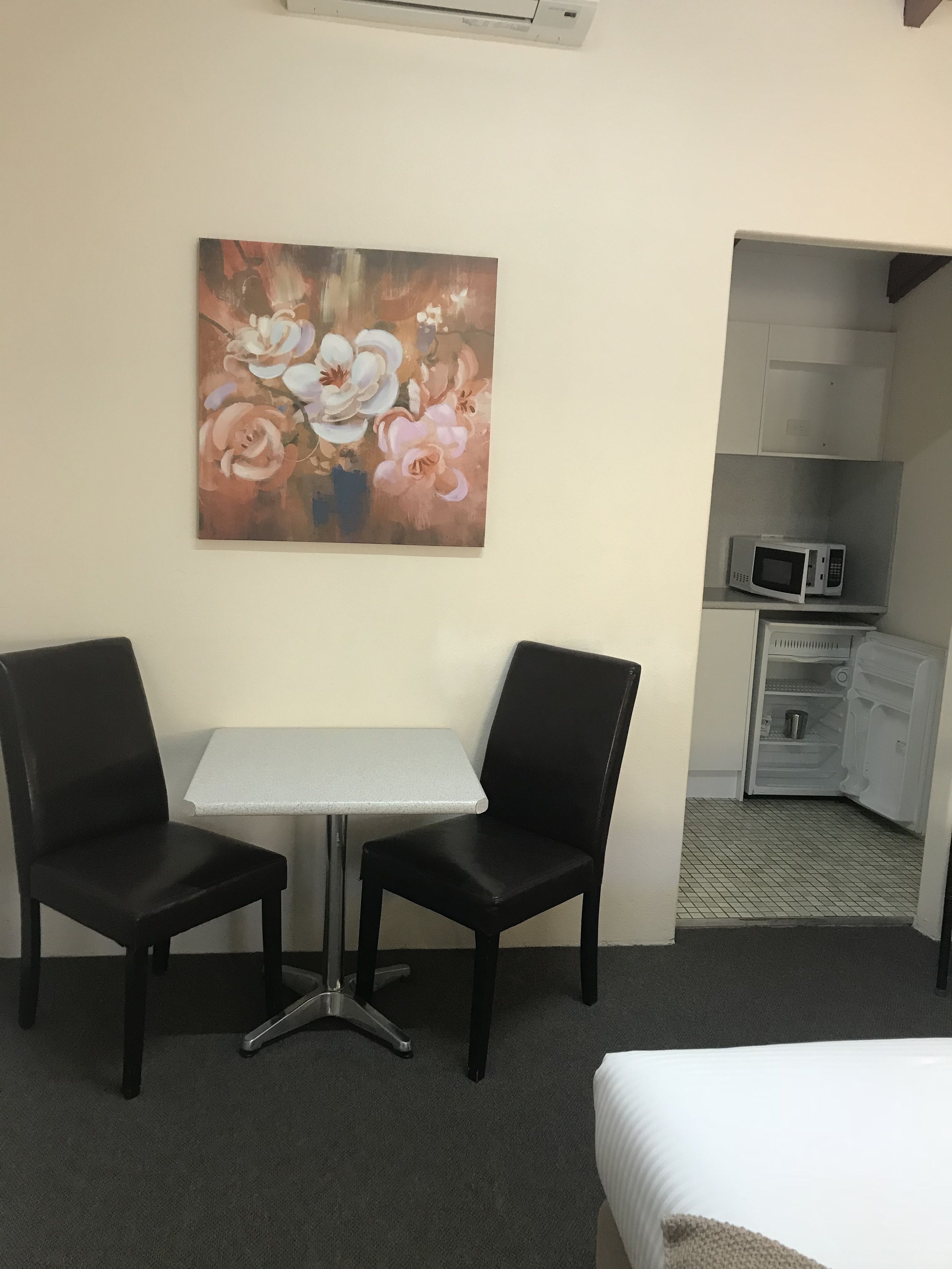 A hotel room with a bed, a small table, two chairs, a microwave, and a painting on the wall.