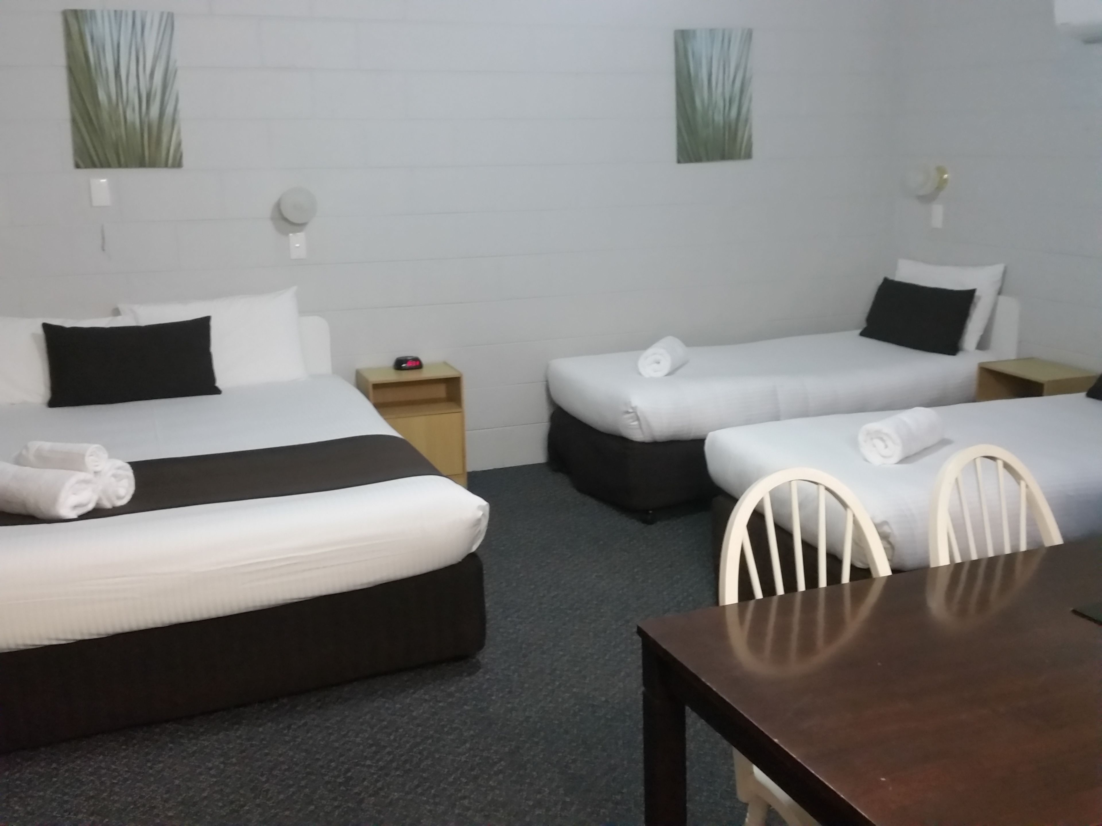 A hotel room with two single beds, a wooden nightstand, a small table, and a chair.