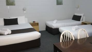 A hotel room with two single beds, a wooden nightstand, a small table, and a chair.