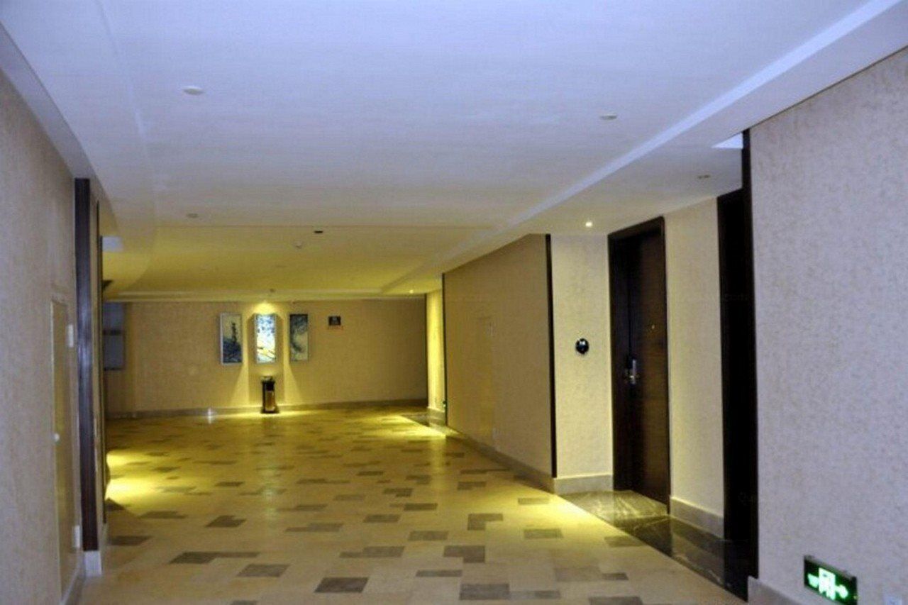 Un couloir d’hôtel avec un sol à carreaux, des portes sur le côté droit et une source de lumière au fond.