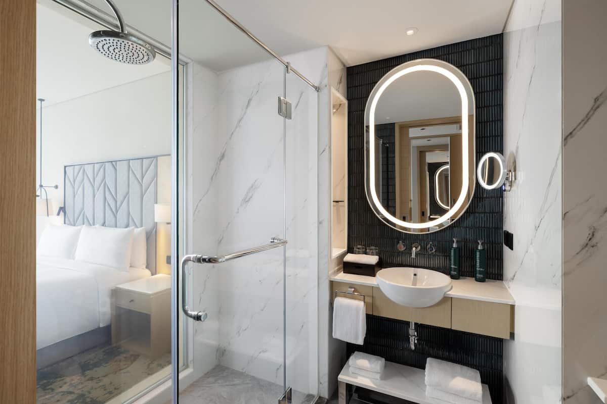 A modern bathroom with a glass shower enclosure, a large mirror with a light, and a marble-tiled vanity.