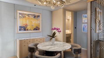 Uma sala de jantar com mesa de mármore, cadeiras estofadas, um vaso com flores cor-de-rosa e um grande quadro abstrato na parede.