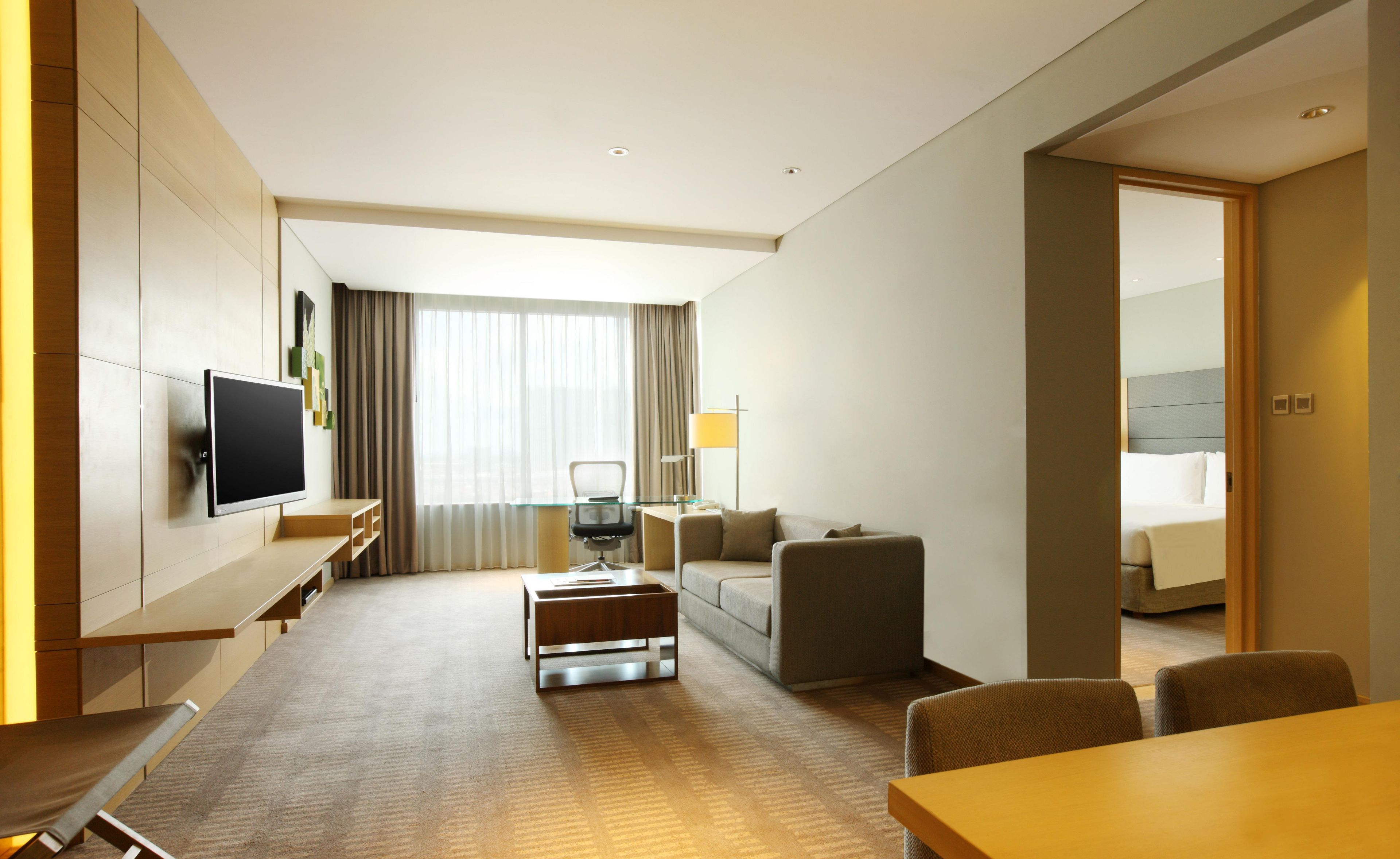 Habitación de hotel con una televisión de pantalla plana montada en la pared, un sofá, una mesa de centro, un escritorio con una silla y una cama con cabecero.