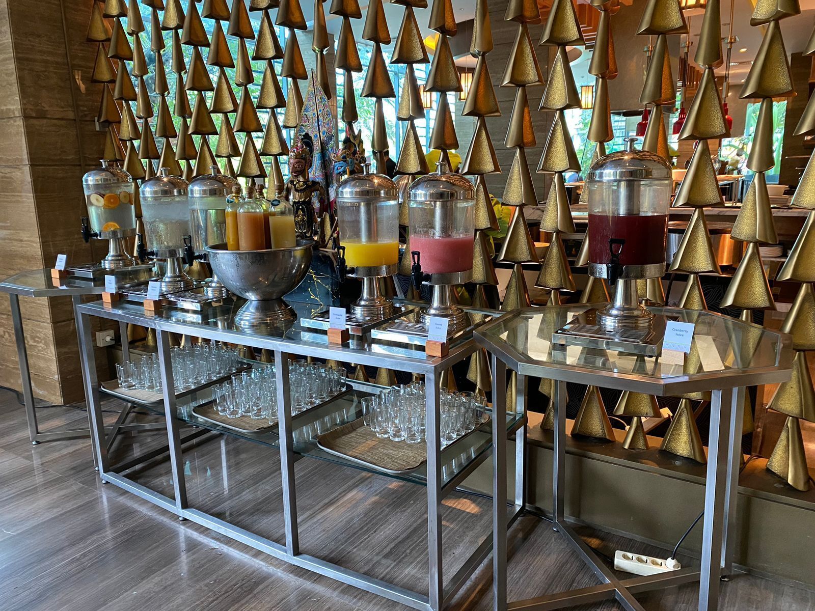 Zona de bufé con varios dispensadores de bebidas y una pared decorativa de conos dorados.