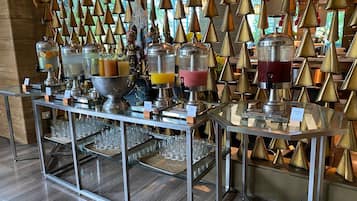 Zona de bufé con varios dispensadores de bebidas y una pared decorativa de conos dorados.