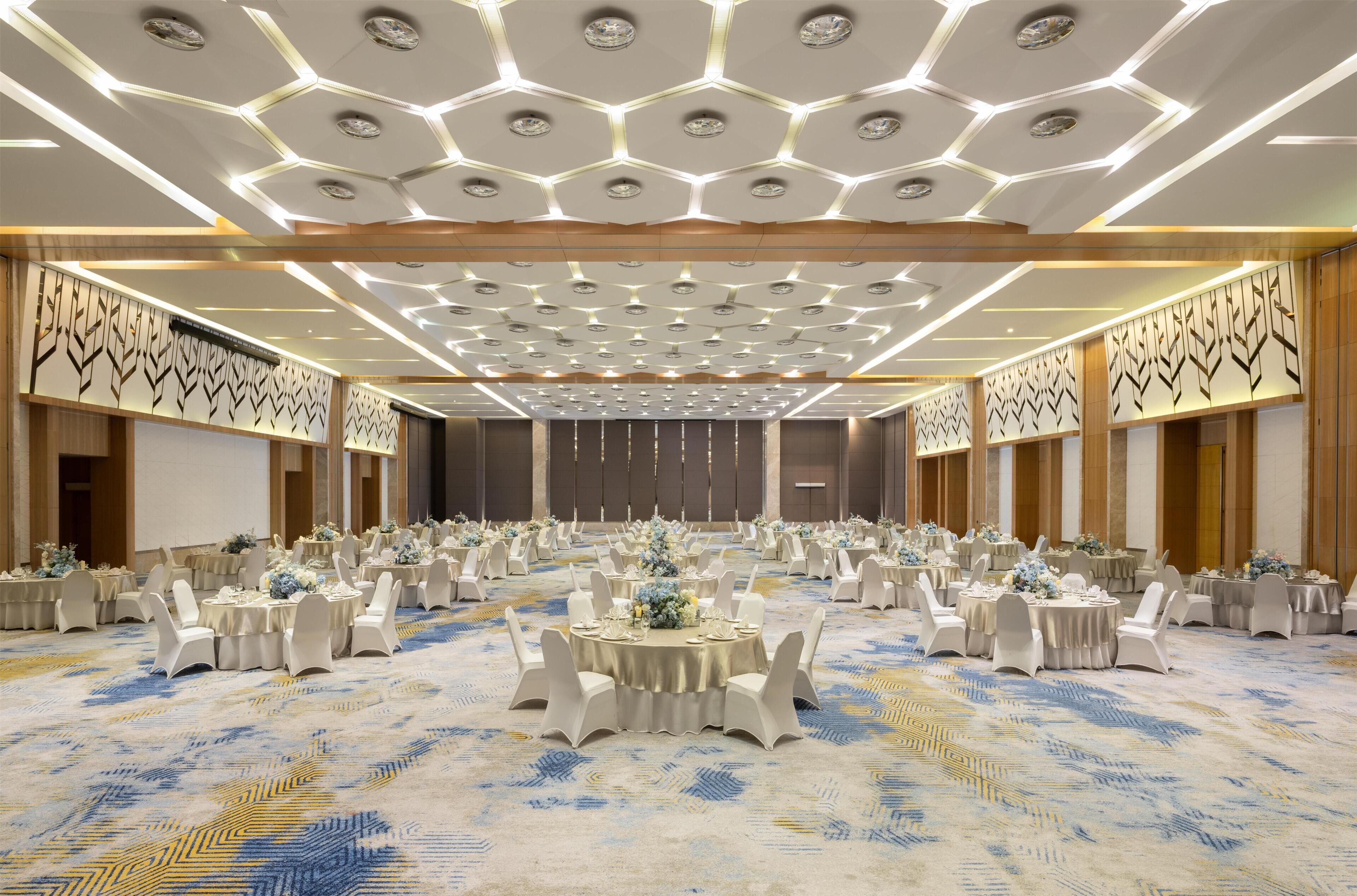 A large banquet hall with round tables, white chairs, and a patterned carpet.
