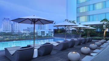 Area piscina sul tetto con poltronne e ombrelloni, vista sulla città.