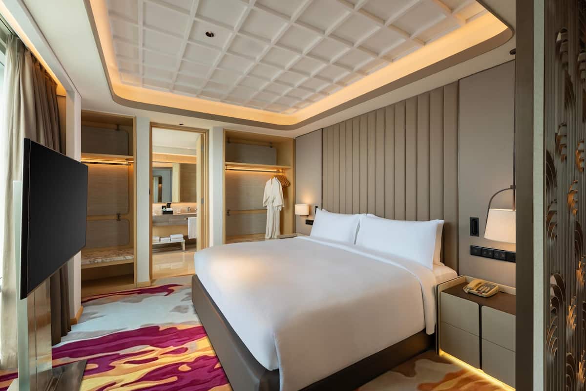 A hotel room with a large bed, a TV, a walk-in closet, and a bathroom with a shower and a towel rack.