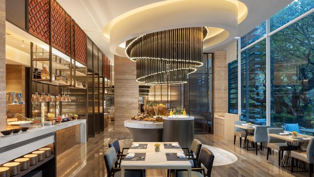 Un restaurante moderno con un área de comedor central, una barra y una cocina visible a través de un separador de vidrio.