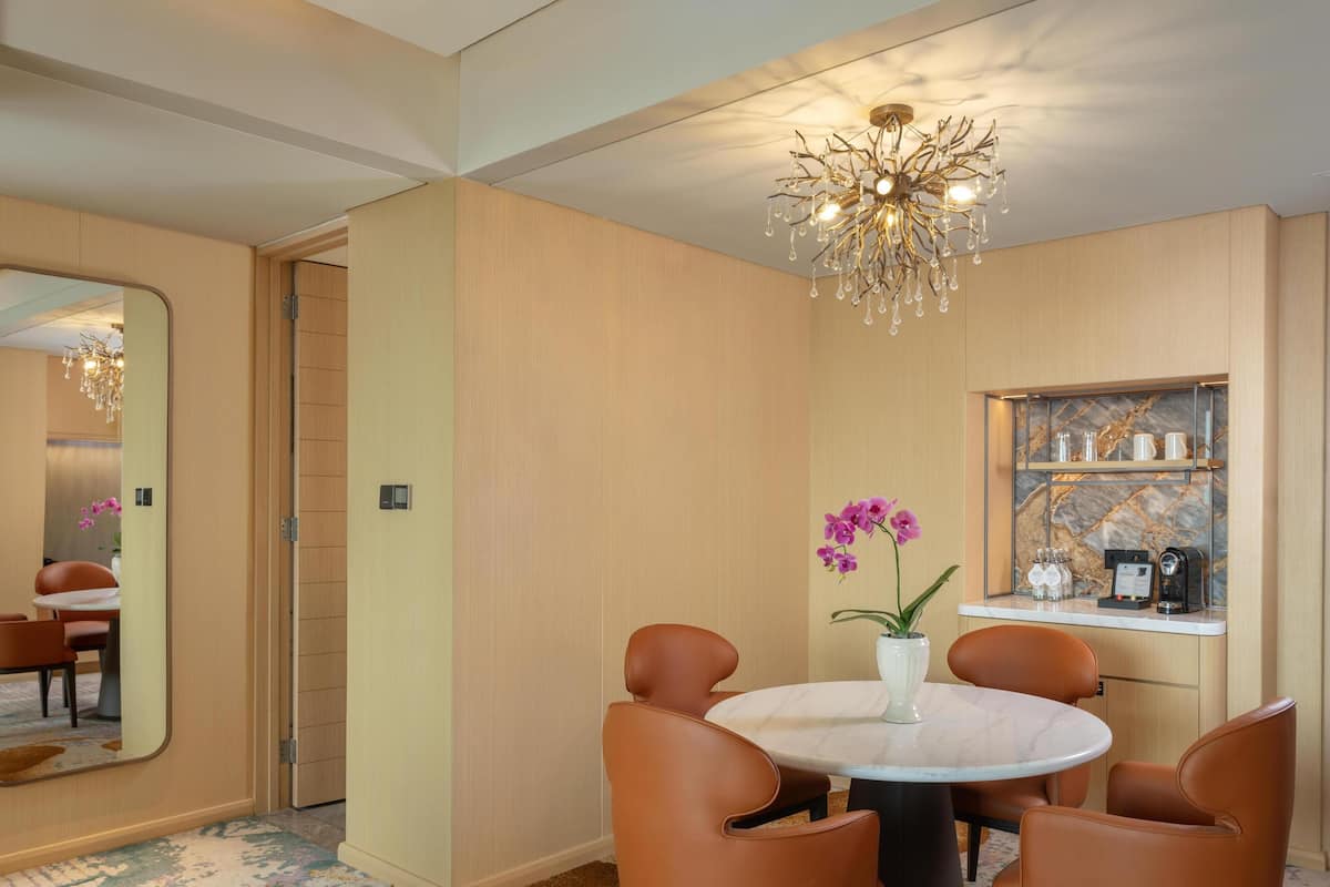A modern dining area with a round table, four brown chairs, a vase with purple flowers, and a chandelier.