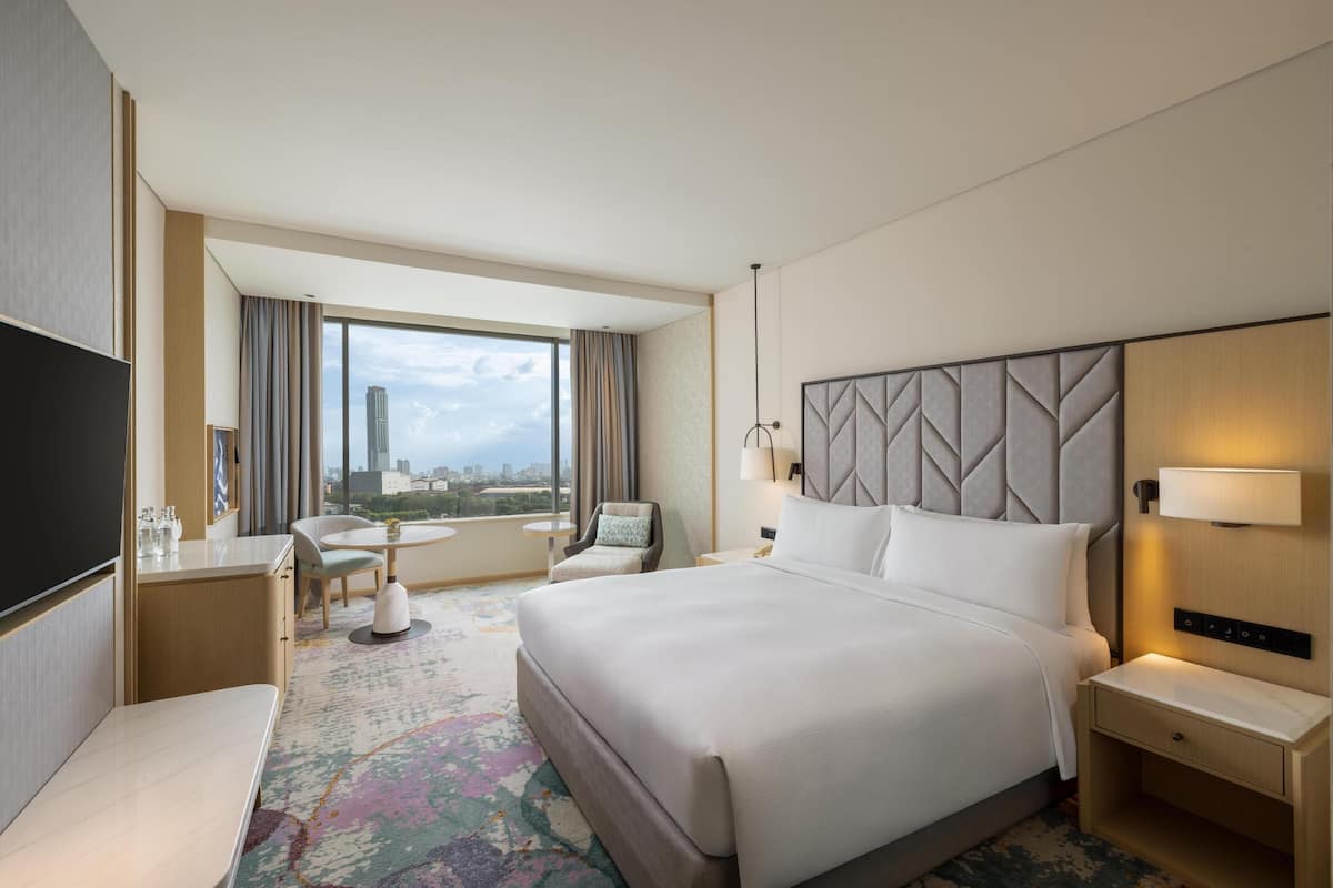 A hotel room with a large bed, a desk, a chair, a small table, and a TV.